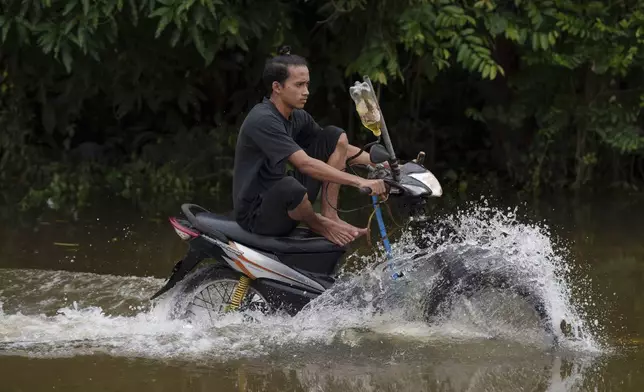 A residents rides a self modified motorcycle through a road covered by flood water in Tumpat, outskirts of Kota Bahru, Malaysia, Tuesday, Dec. 3, 2024. (AP Photo/Vincent Thian)