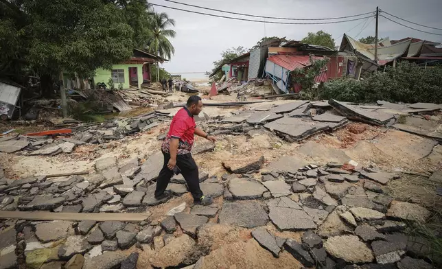 A resident crosses a road past houses damaged by flood in Tumpat, outskirts of Kota Bahru, Malaysia, Tuesday, Dec. 3, 2024. (AP Photo/Vincent Thian)