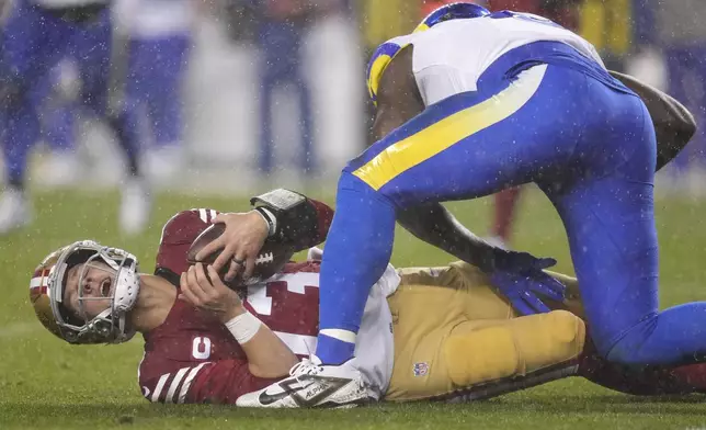 San Francisco 49ers quarterback Brock Purdy, bottom, reacts after being sacked by Los Angeles Rams defensive tackle Kobie Turner, top, during the first half of an NFL football game in Santa Clara, Calif., Thursday, Dec. 12, 2024. (AP Photo/Godofredo A. Vásquez)