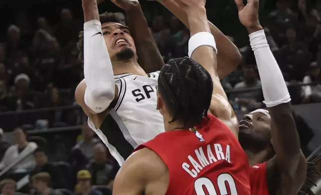 San Antonio Spurs center Victor Wembanyama, left, attempts a shot against Portland Trail Blazers forward Jerami Grant, right, and forward Toumani Camara (33) during the first half of an NBA basketball game in San Antonio, Saturday, Dec. 21, 2024. (AP Photo/Kin Man Hui)