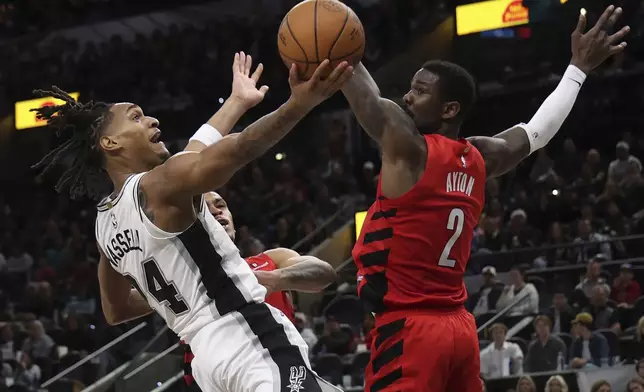 San Antonio Spurs guard Devin Vassell (24) makes a shot attempt against Portland Trail Blazers center Deandre Ayton (2) and forward Toumani Camara, behind Vassell, during the first half of an NBA basketball game in San Antonio, Saturday, Dec. 21, 2024. (AP Photo/Kin Man Hui)