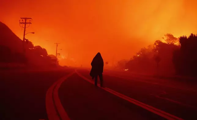 A person walks along a road as the Franklin Fire approaches in Malibu, Calif., Dec. 10, 2024. (AP Photo/Eric Thayer)