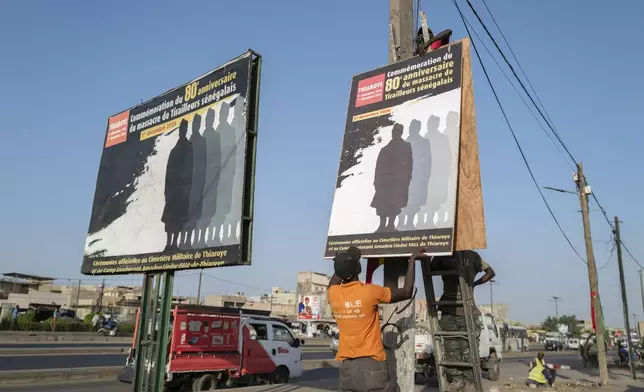 Workers put up a poster marking the 80th anniversary of the Thiaroye massacre Thiaroye, Senegal, Thursday, Nov. 28, 2024. (AP Photo/Sylvain Cherkaoui)