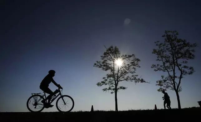 FILE - A cyclist and two joggers in silhouette navigate the bike path along Lake Michigan at the 31st Street Harbor Saturday, May 27, 2023, in Chicago. (AP Photo/Charles Rex Arbogast, File)