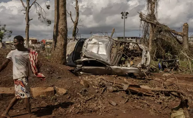 A man walks by a destroyed car in Mirereni, Mayotte, Friday, Dec. 20, 2024. (AP Photo/Adrienne Surprenant)