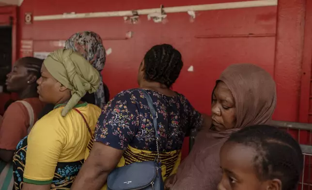 Women wait for supplies to be delivered at a supermarket in Mamoudzou, Mayotte, Friday, Dec. 20, 2024. (AP Photo/Adrienne Surprenant)