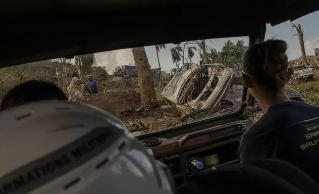 Broken cars litter the road in Mirereni, Mayotte, Friday, Dec. 20, 2024. (AP Photo/Adrienne Surprenant)