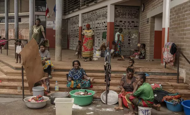 Women wash clothes after a short rain filled their pots with water, at the Lycée des Lumières where they found shelter after losing their homes, in Mamoudzou, Mayotte, Thursday, Dec. 19, 2024 . (AP Photo/Adrienne Surprenant)