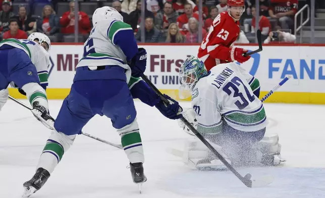 Vancouver Canucks defenseman Erik Brannstrom (26) stops a shot that got past goaltender Kevin Lankinen (32) with Detroit Red Wings left wing Lucas Raymond (23) looking on during the first period of an NHL hockey game Sunday, Dec. 1, 2024, in Detroit. (AP Photo/Duane Burleson)