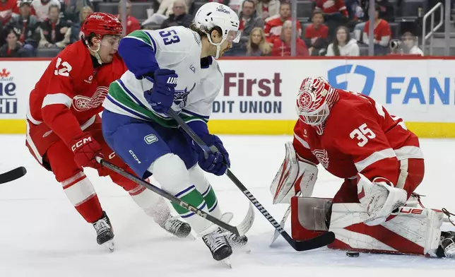 Detroit Red Wings goaltender Ville Husso (35) stop a shot-attempt by Vancouver Canucks center Teddy Blueger (53) with Red Wings center Marco Kasper, left, helping defend during the second period of an NHL hockey game Sunday, Dec. 1, 2024, in Detroit. (AP Photo/Duane Burleson)