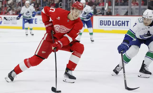 Detroit Red Wings defenseman Simon Edvinsson (77) takes a shot on goal against Vancouver Canucks defenseman Carson Soucy (7) during the first period of an NHL hockey game Sunday, Dec. 1, 2024, in Detroit. (AP Photo/Duane Burleson)