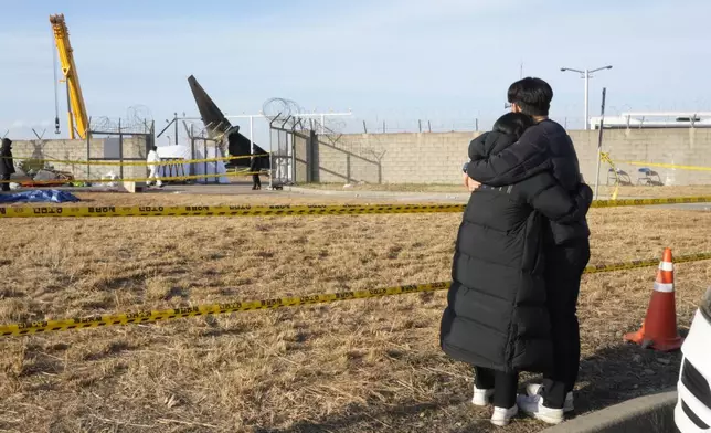 Mourners watch the site of a plane fire from outside of Muan International Airport in Muan, South Korea, Monday, Dec. 30, 2024. (AP Photo/Ahn Young-joon)