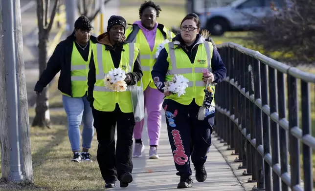 A group makes their way to leave flowers outside the Abundant Life Christian School Tuesday, Dec. 17, 2024 in Madison, Wis., following a shooting on Monday. (AP Photo/Morry Gash)