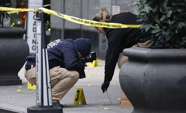 Members of the New York police crime scene unit photograph bullets lying on the sidewalk as they investigate the scene outside the Hilton Hotel in midtown Manhattan where Brian Thompson, the CEO of UnitedHealthcare, was fatally shot, Wednesday, Dec. 4, 2024, in New York. (AP Photo/Stefan Jeremiah)