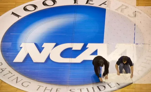 FILE - Wachovia Center operations manager Jim McDonald, left, and carpenter foreman Tim Allen remove the protective film covering the NCAA logo at mid-court on the center's basketball court, Wednesday, March 15, 2006, in Philadelphia. NCAA athletes will be immediately eligible to play no matter how many times they transfer — as long as they meet academic requirements — after the association fast-tracked legislation Wednesday, April 17, 2024, to fall in line with a recent court order. (Ed Hille/The Philadelphia Inquirer via AP, File)