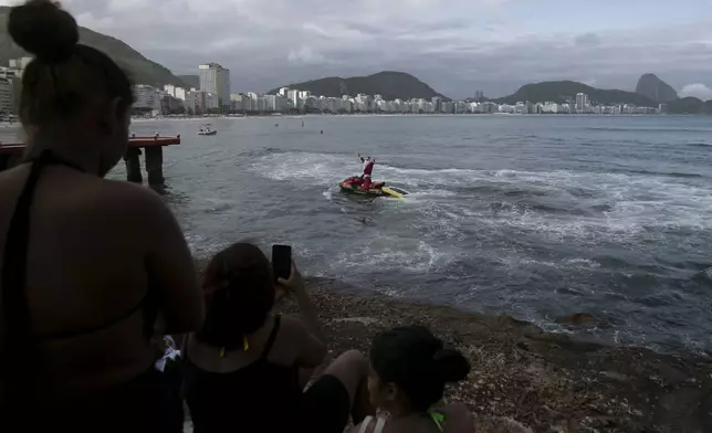 A firefighter dressed as Santa Claus waves from a Jet Ski off of Copacabana Beach in Rio de Janeiro, Tuesday, Dec. 17, 2024. (AP Photo/Bruna Prado)