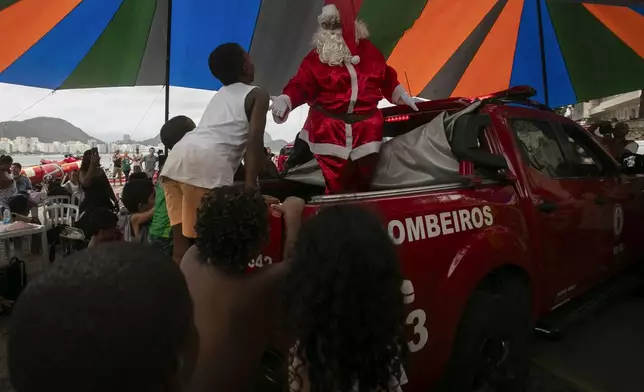 A firefighter dressed as Santa Claus entertains children on Copacabana Beach in Rio de Janeiro, Tuesday, Dec. 17, 2024. (AP Photo/Bruna Prado)