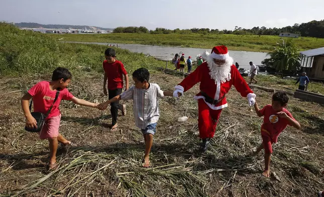 Jorge Barroso, dressed as Santa Claus, is received by young residents after arriving on a boat to distribute Christmas gifts to children who live in the riverside communities of the Amazon, in Iranduba, Brazil, Saturday, Dec. 21, 2024. (AP Photo/Edmar Barros)