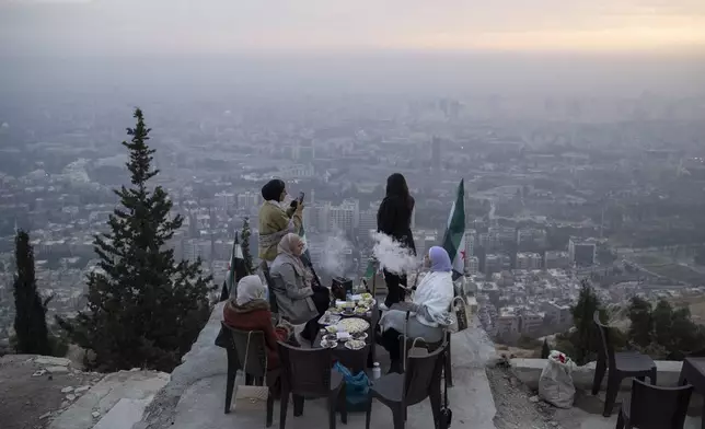 Women smoke water pipe as they sit on a lookout area at the mount Qasioun in Damascus, Syria, Saturday, Dec. 21, 2024. (AP Photo/Leo Correa)