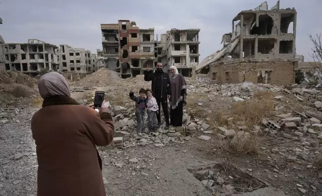 A Syrian man Mohammed Salam, 32, poses for a picture with his family in front of his destroyed house which destroyed during the civil war in the neighbourhood of Jobar, in Damascus, Syria, Saturday, Dec. 21, 2024. (AP Photo/Hussein Malla)