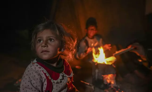 The grandchildren of Reda Abu Zarada sit by a fire at a camp by the sea in Khan Younis, Gaza Strip, Thursday, Dec. 19, 2024. (AP Photo/Abdel Kareem Hana)