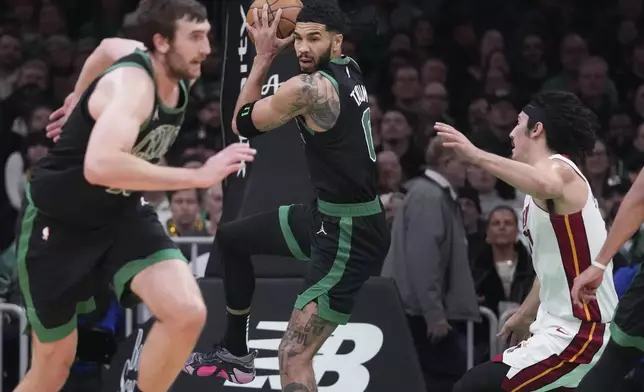 Boston Celtics forward Jayson Tatum, center, grabs a rebound against Miami Heat guard Jaime Jaquez Jr., right, during the first half of an NBA basketball game, Monday, Dec. 2, 2024, in Boston. (AP Photo/Charles Krupa)