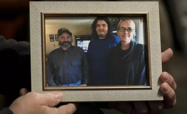 Jerry Barnett holds a picture of, from left, himself; his son, Caimen; and his wife, Sibrina; Nov. 22, 2024, in Johnson City, Tenn. Barnett's wife died trying to escape flood waters caused by Hurricane Helene in September, near the plastics factory where she cleaned offices once a week. (AP Photo/George Walker IV)