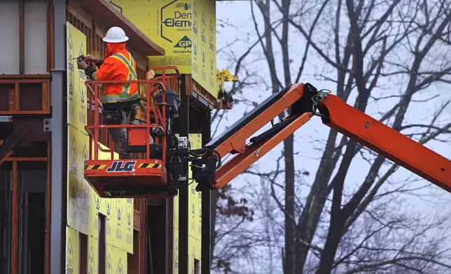 A construction worker is bundled up in winter clothes while installing weather sheathing on a building during a rain storm, Wednesday, Dec. 11, 2024, in Derry, N.H. (AP Photo/Charles Krupa)