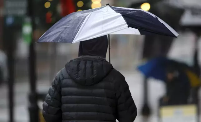 A person walks through the rain as a storm system and possible "bomb cyclone" hit the U.S. East Coast, Wednesday, Dec. 11, 2024 in Portsmouth, N.H. (AP Photo/Caleb Jones)