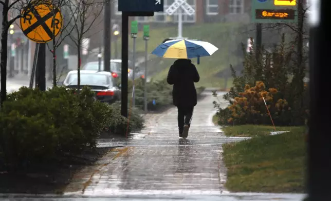 A person walks through the rain as a storm system and possible "bomb cyclone" hit the U.S. East Coast, Wednesday, Dec. 11, 2024 in Portsmouth, N.H. (AP Photo/Caleb Jones)