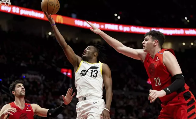 Utah Jazz guard Isaiah Collier, middle, drives to the hoop against Portland Trail Blazers center Donovan Clingan, right, during the second half of an NBA basketball game Thursday, Dec. 26, 2024, in Portland, Ore. (AP Photo/Howard Lao)