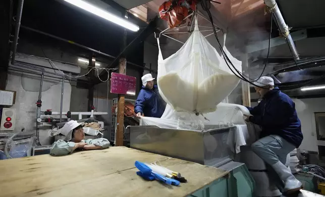 Sake brewer Mie Takahashi, from left, watches her crew Shigeru Kikuchi and Daichi Ushiyama use a crane to move steamed sake rice into another unit in a Japanese sake making process at her Koten sake brewery in Okaya, central Japan, Saturday, Nov. 30, 2024. (AP Photo/Hiro Komae)