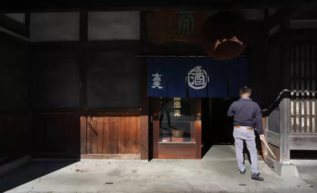 Isao Takahashi, president of the Koten sake brewery, puts up a "noren," a short curtain hung in front of a company entrance in Okaya, central Japan, Saturday, Nov. 30, 2024. (AP Photo/Hiro Komae)