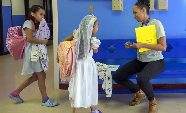 Attendance Clerk Katrice Grant speaks to siblings Melanie Pacheco, 8, left, and Marilynn Pacheco, 5, in the hallway before heading to their classrooms, Tuesday, Oct. 1, 2024, at Algodones Elementary School in Algodones, N.M. (AP Photo/Roberto E. Rosales)