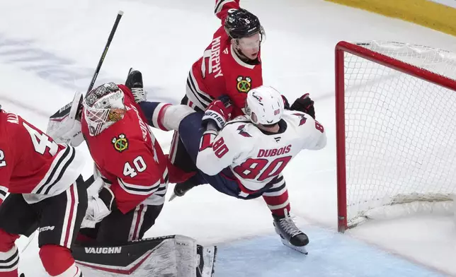 Chicago Blackhawks' Connor Murphy (5) knocks Washington Capitals' Pierre-Luc Dubois to the ice behind goaltender Arvid Soderblom during the third period of an NHL hockey game Tuesday, Dec. 17, 2024, in Chicago. (AP Photo/Charles Rex Arbogast)