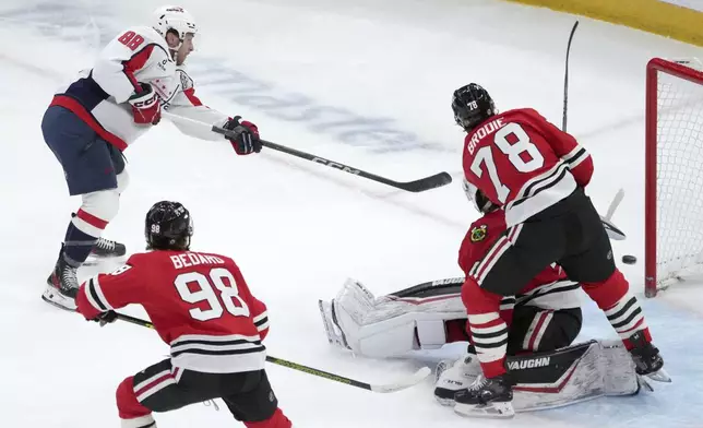 Washington Capitals' Andrew Mangiapane (88) scores past Chicago Blackhawks goaltender Arvid Soderblom as TJ Brodie (78) also defends during the first period of an NHL hockey game Tuesday, Dec. 17, 2024, in Chicago. (AP Photo/Charles Rex Arbogast)