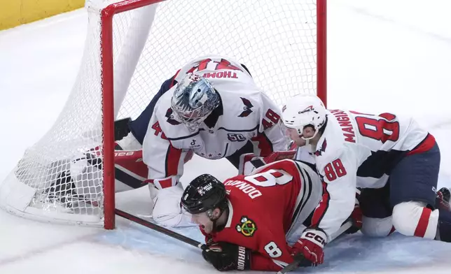 Chicago Blackhawks' Ryan Donato (8) falls to the ice after scoring past Washington Capitals' Logan Thompson and Andrew Mangiapane during the third period of an NHL hockey game Tuesday, Dec. 17, 2024, in Chicago. (AP Photo/Charles Rex Arbogast)