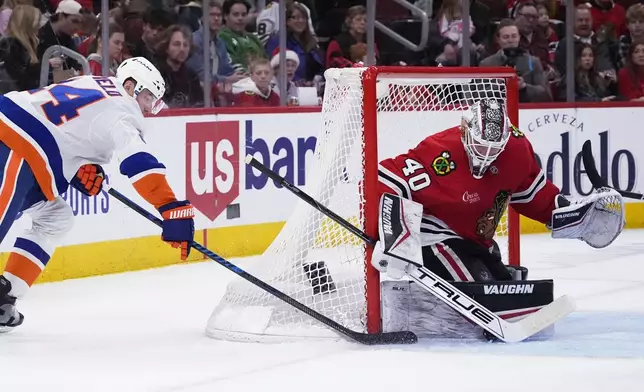 Chicago Blackhawks goaltender Arvid Soderblom, right, stops a shot by New York Islanders defenseman Scott Mayfield, left, during the second period of an NHL hockey game in Chicago, Sunday, Dec. 15, 2024. (AP Photo/Nam Y. Huh)