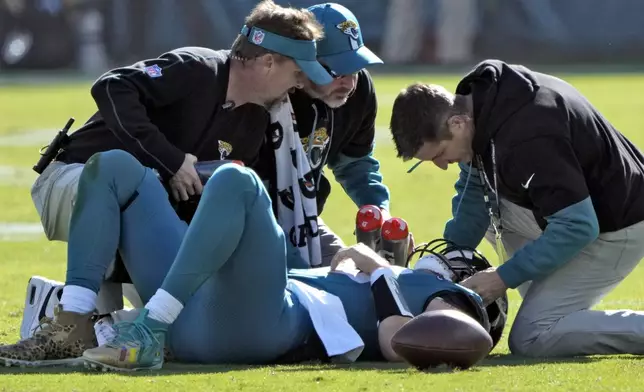 Jacksonville Jaguars quarterback Trevor Lawrence (16) is looked at by trainers after a late hit by Houston Texans linebacker Azeez Al-Shaair (0) during the first half of an NFL football game Sunday, Dec. 1, 2024, in Jacksonville, Fla. (AP Photo/John Raoux)