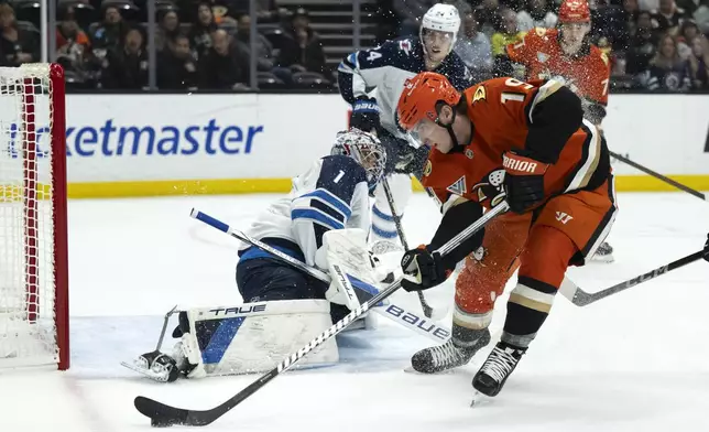 Anaheim Ducks right wing Troy Terry (19) controls the puck in front of Winnipeg Jets goaltender Eric Comrie (1) during the first period of an NHL hockey game, Wednesday, Dec. 18, 2024, in Anaheim, Calif. (AP Photo/Kyusung Gong)