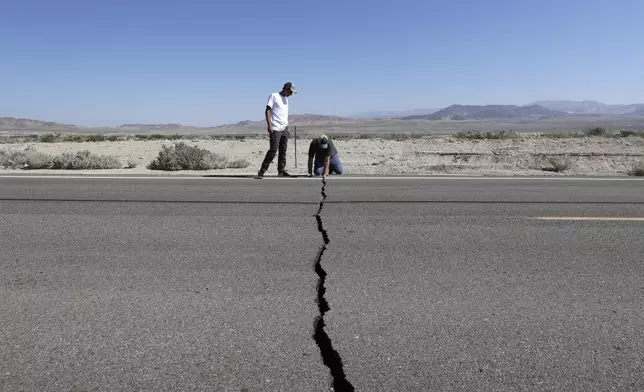 FILE - Ron Mikulaco, right, and his nephew, Brad Fernandez, examine a crack caused by an earthquake on Highway 178, on July 6, 2019, outside of Ridgecrest, Calif. (AP Photo/Marcio Jose Sanchez, File)