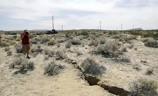 FILE - In this July 7, 2019 file photo, a visitor takes a photo of a crack in the ground following earthquakes near Ridgecrest, Calif. (AP Photo/Marcio Jose Sanchez, File)