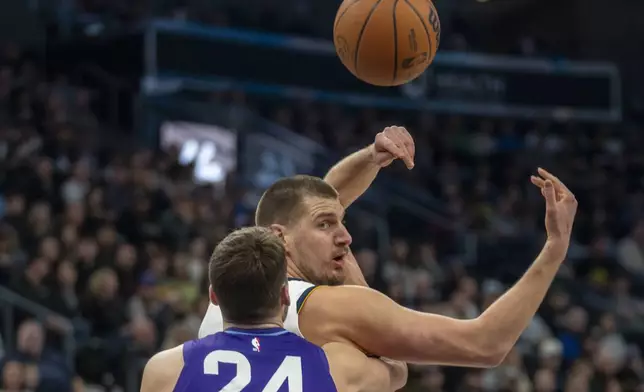 Denver Nuggets center Nikola Jokic, top, tosses a pass over his shoulder as Utah Jazz center Walker Kessler (24) defends during the first half of an NBA basketball game Monday, Dec. 30, 2024, in Salt Lake City. (AP Photo/Rick Egan)