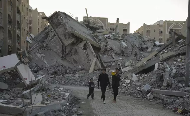 Young Palestinians walk amongst rubble of destroyed buildings at a neighbourhood in Khan Younis, Gaza Strip, Sunday, Dec. 1, 2024. (AP Photo/Abdel Kareem Hana)