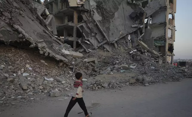 A Palestinian boy walks past destroyed building at a neighbourhood in Khan Younis, Gaza Strip, Sunday, Dec. 1, 2024. (AP Photo/Abdel Kareem Hana)