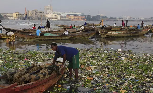 FILE - In this Nov. 17, 2011 file photo, a fisherman stands amidst city trash brought in by the tide, as he prepares to launch his fishing boat, in Cotonou, Benin. (AP Photo/Rebecca Blackwell, File)