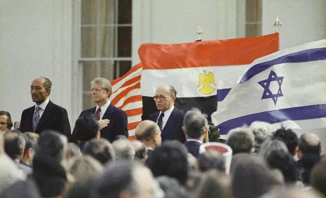 FILE - U.S. President Jimmy Carter, center, Egyptian President Anwar Sadat, left, and Israeli Prime Minister Menachem Begin stand in front of the billowing national flags of the U.S., Egypt and Israel, as the national anthems are played before the signing of the peace treaty between Israel and Egypt at the White House in Washington, March 26, 1979. (AP Photo, File)