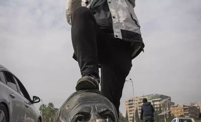 An opposition fighter steps on a broken bust of the late Syrian President Hafez Assad in Damascus, Syria, Sunday Dec. 8, 2024. (AP Photo/Hussein Malla)