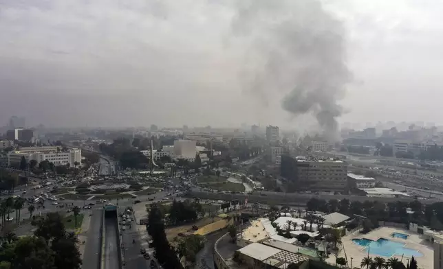 Smoke billows in the background as residents and opposition fighters celebrate in a central square after opposition forces took control of the city in Damascus, Syria, Sunday, Dec. 8, 2024. (AP Photo/Ghaith Alsayed)
