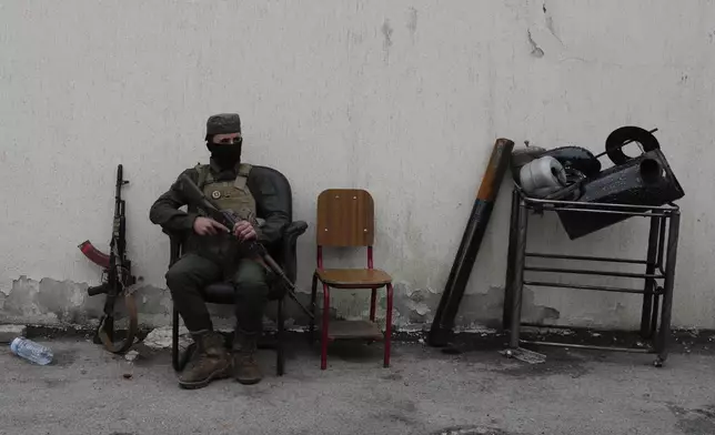 A member of the security forces of the newly formed Syrian government looks on as members of Bashar Assad's army, or a pro-government militia, line up to register as part of an "identification and reconciliation" process in Damascus, Syria, Monday, Dec. 30, 2024. (AP Photo/Omar Sanadiki)